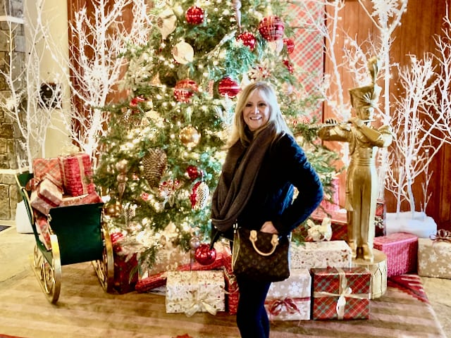 Holiday gifts and a woman standing in front of a Christmas tree.