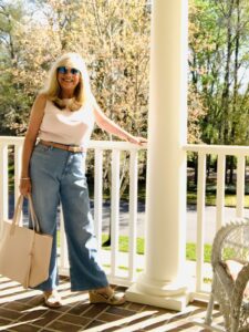 Woman standing on a porch wearing wide leg jeans and earring a pink handbag