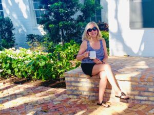 A blonde woman wearing sunglasses sitting on the front porch