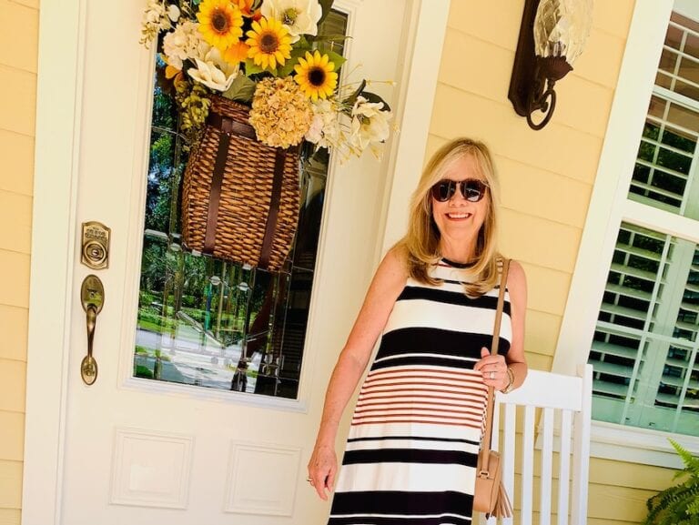 Woman standing at the front door wearing a casual summer dress and sunglasses.