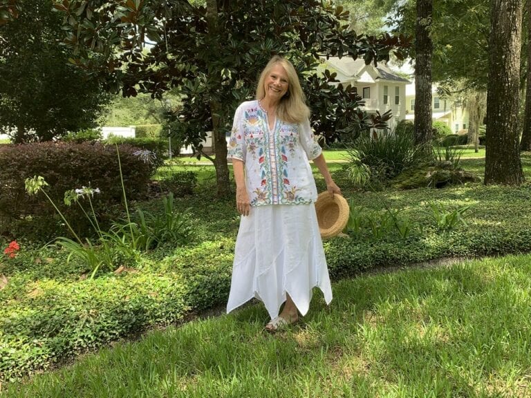 Woman standing under the trees wearing a white boho-chic vacation outfit