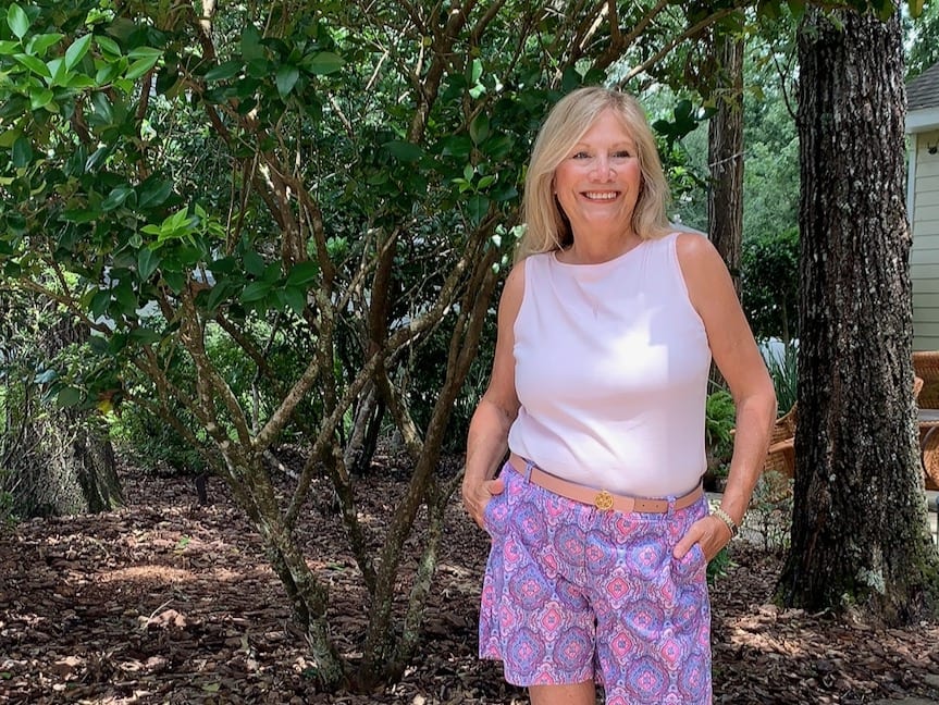 Woman standing under the trees wearing shorts and a sleeveless tee!