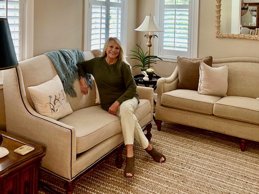 Woman sitting on a sofa wearing a green sweatshirt and light colored slacks