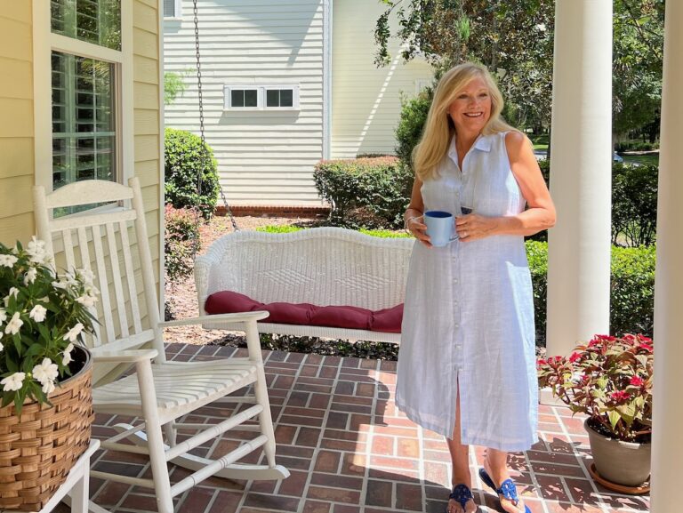 Woman standing on a front porch with a coffee cup.
