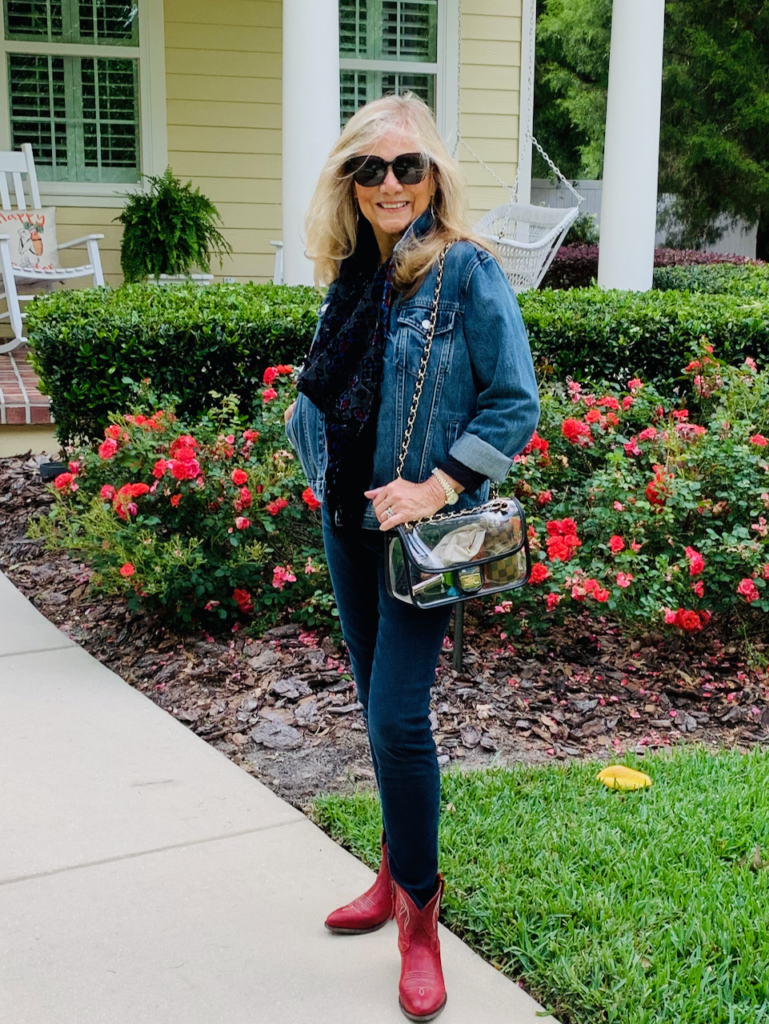 A blonde woman wearing a denim jacket with blue jeans and red cowboy boots is dressed in a style of southwestern vibes for Fall.