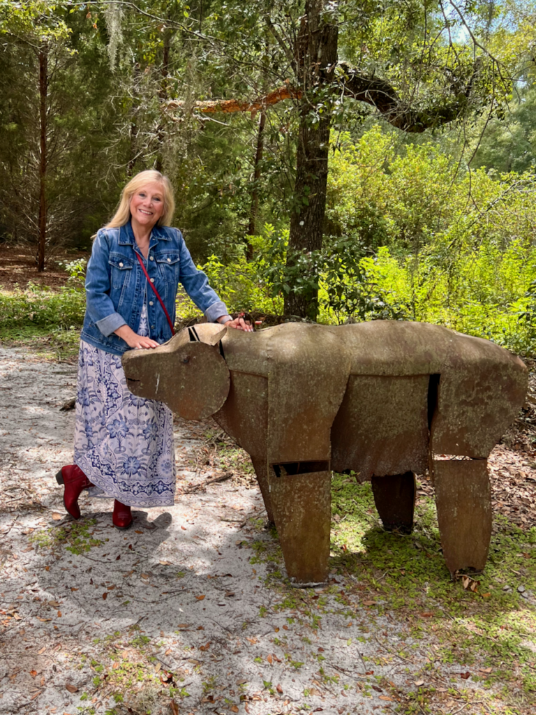 A blonde woman standing beside a metal sculpture of a bear. She is dressed in a style of southwestern vibes for Fall.