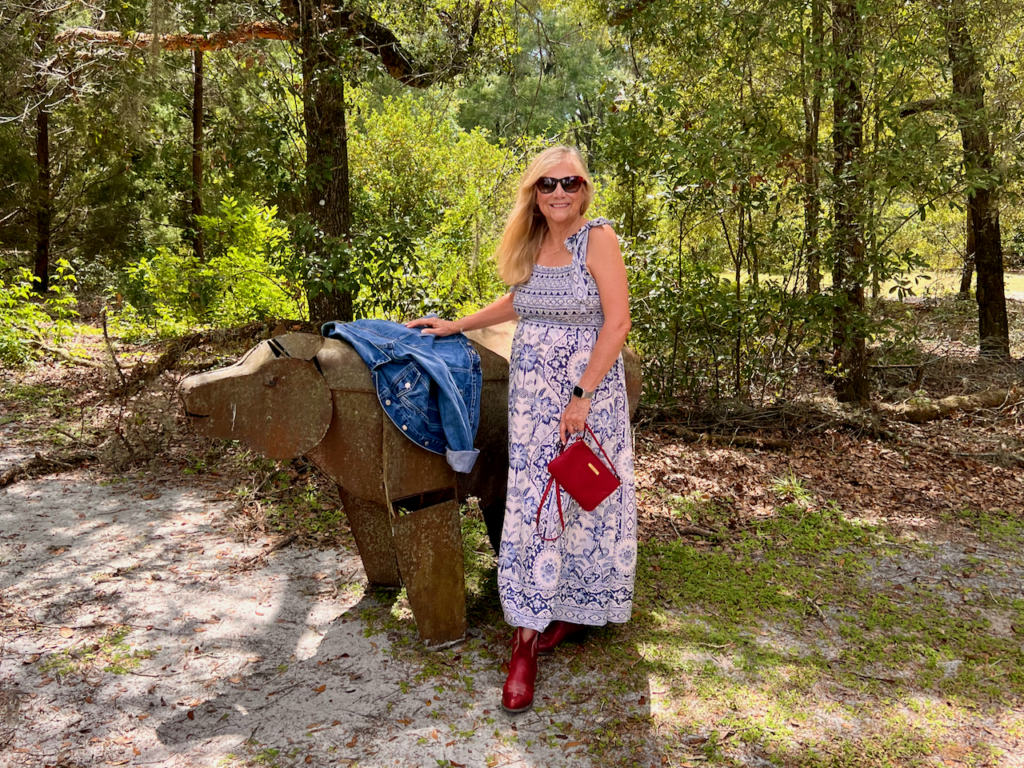 A blonde woman is standing beside a metal sculpture of a bear. She is dressed in a style of southwestern vibes for Fall.