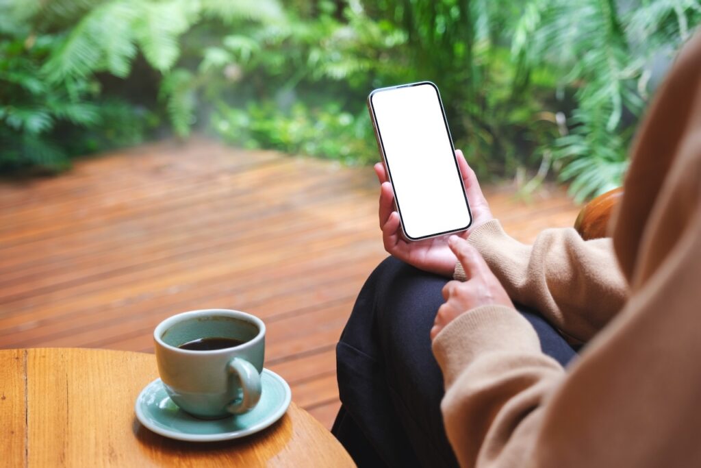 An image of a woman holding a mobile phone with a blank white desktop screen in the garden.