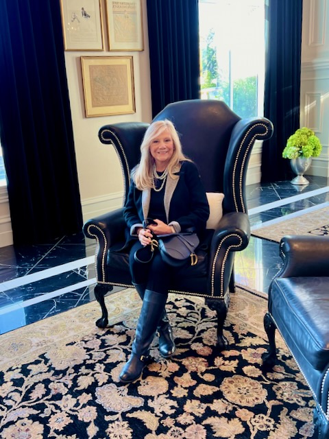 A blonde woman sits in a black leather chair in the hotel lobby. 