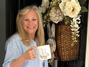 A Blonde woman steps out of a door with a coffee cup in her hand. March Coffee Chat