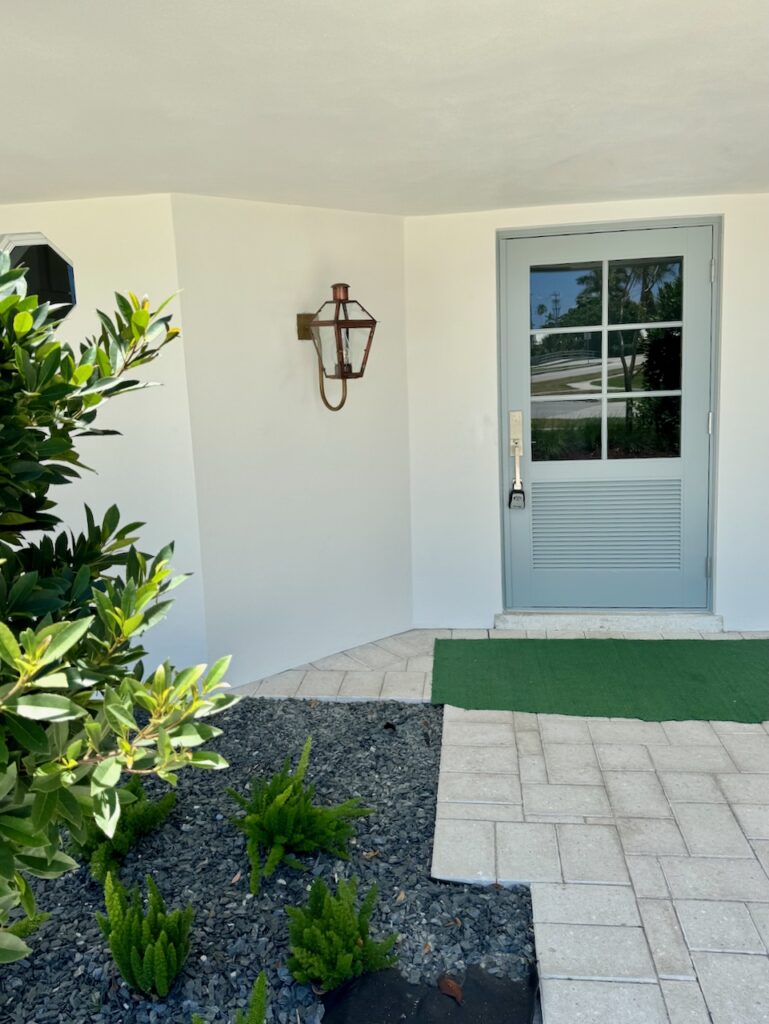 A blue-gray front door and brass sconce lantern.