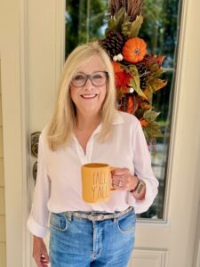 Blonde woman standing at the front door with a cup of coffee.