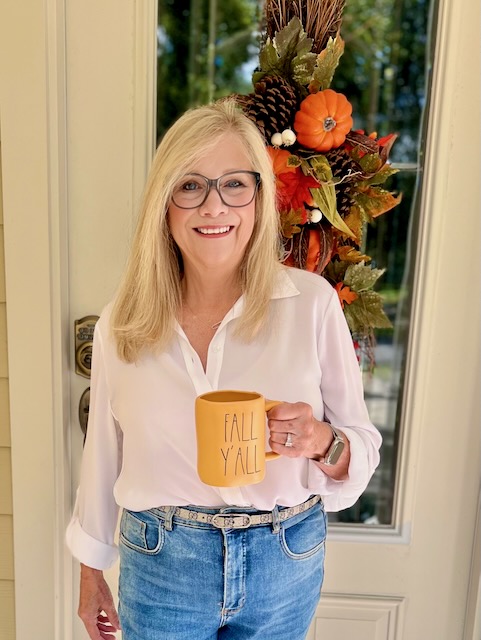 Blonde woman standing at the front door with a cup of coffee.