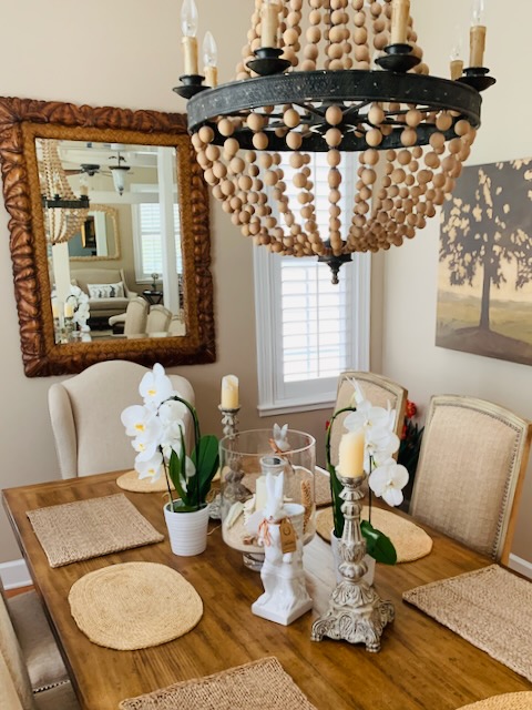 A Southern dining room featuring a chandelier made of metal and wooden balls. Plus a carved wooden rectangular mirror.