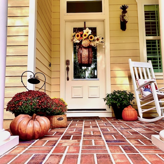 A southern-style front porch decorated for fall with pumpkins and flowers.