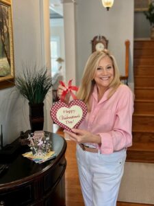Blonde woman wearing a pink shirt and holding a Happy Valentine's Day heart.