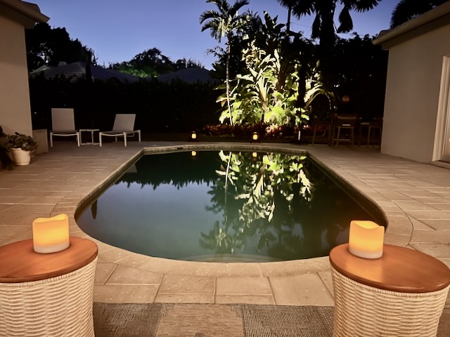 View of the pool from the lanai. Landscape lighting and candles are lighting up the scene.