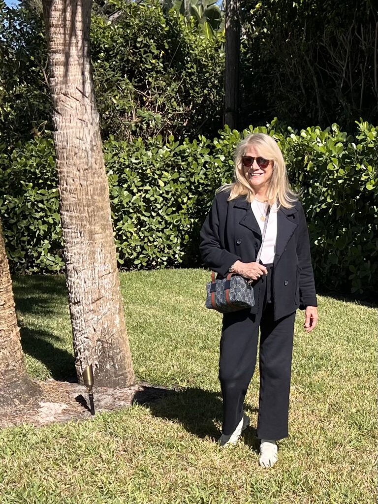Blonde woman walking on a green lawn. She is wearing a navy blazer, sweatpants, and white top.